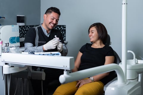 Male dentist in gloves examines female patient in dental chair in modern clinic with blue-gray walls