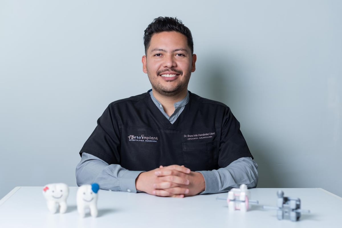 Man in medical scrubs at a desk with dental models and medical instruments against a light blue background
