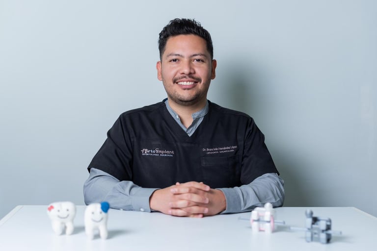 Man in medical scrubs at a desk with dental models and medical instruments against a light blue background