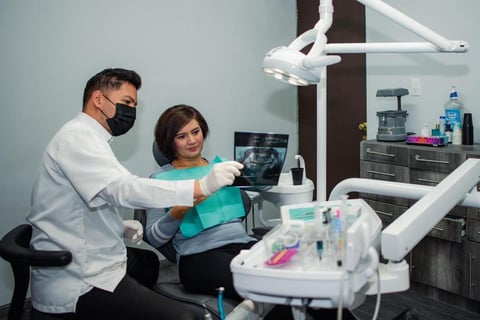 Dentist and dental assistant discussing X-ray image on tablet in modern dental operatory with equipment visible
